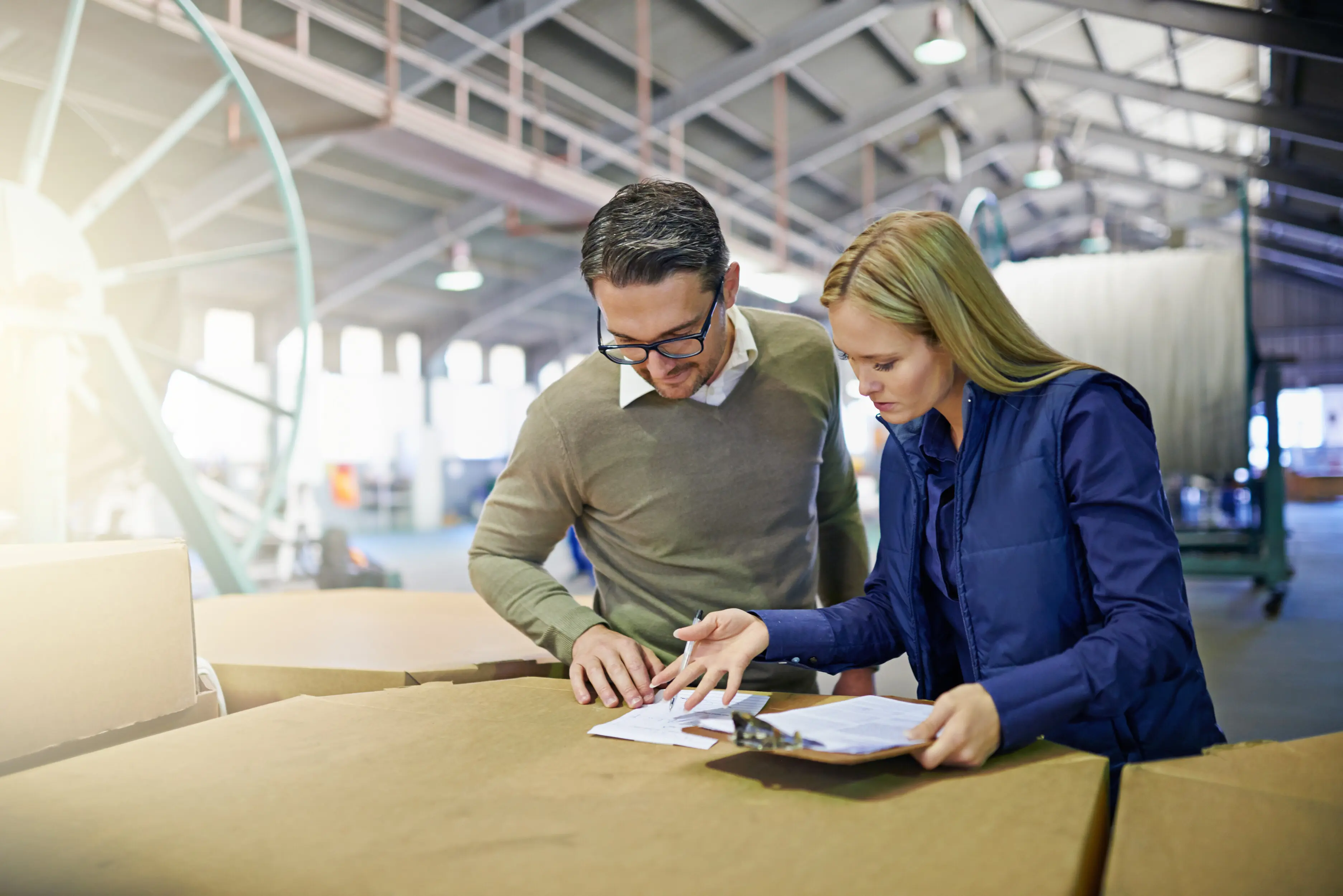Business professionals reviewing and verifying inventory in warehouse storage using a supply chain checklist, with coworkers or employees looking at documents, paperwork, or a clipboard in factory distribution.